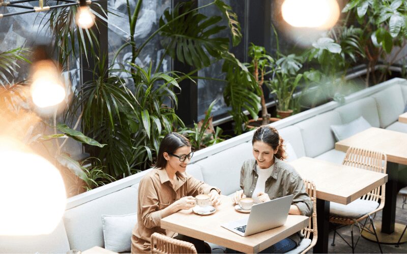 herramientas de automatización del marketing: imagen de dos mujeres de negocios charlando en una mesa mirando la pantalla de un portátil