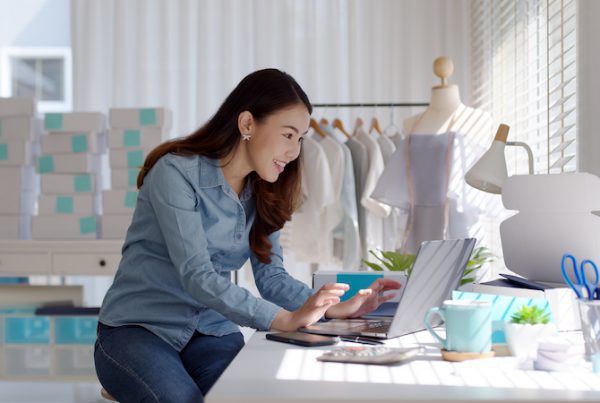 Automação para e-commerce: imagem de uma mulher asiática digitando em um notebook com caixas de encomendas ao fundo