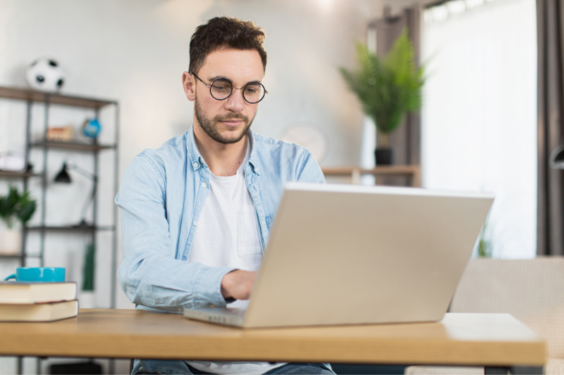 transformação digital: imagem de um homem jovem com óculos e camisa azul, digitando em um notebook prata numa sala de escritório