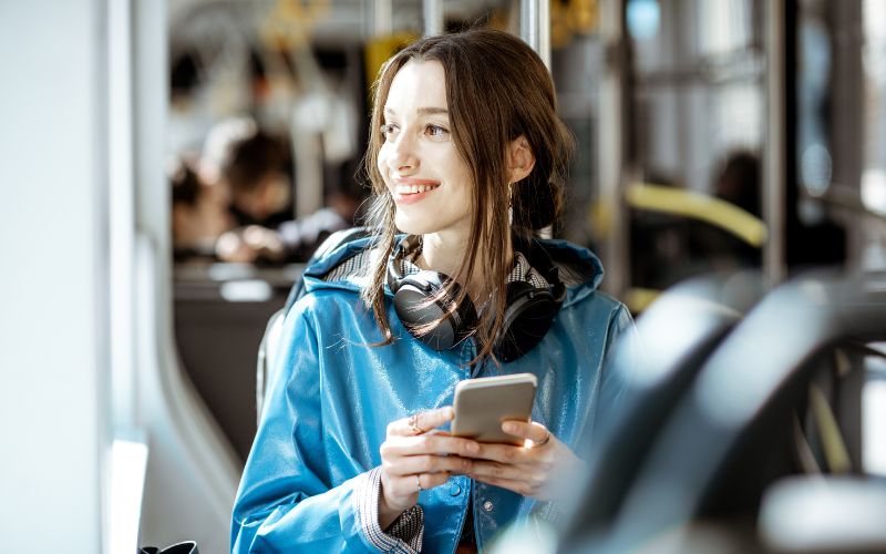 Mobees: imagem de uma mulher dentro de um transporte público olhando para janela e mexendo no celular