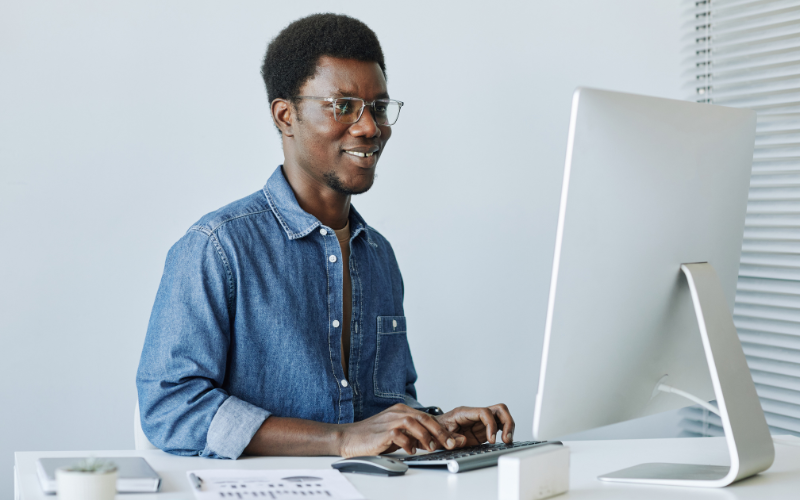 google performance max: imagem de um homem negro usando óculos e caminha social em um escritório digitando no teclado e olhando para tela do computador