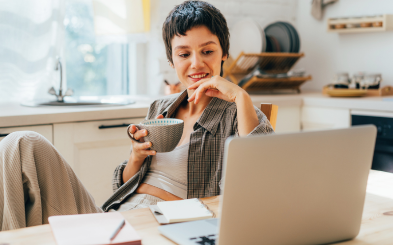 Criar Videos: mulher de cabelo curto, sentada em frente ao seu computador, com uma xícara de chá em mãos