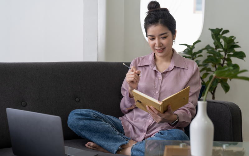 Aplicações da Inteligência Artificial: imagem de uma jovem asiática sentada no sofá, olhando para o seu caderno.