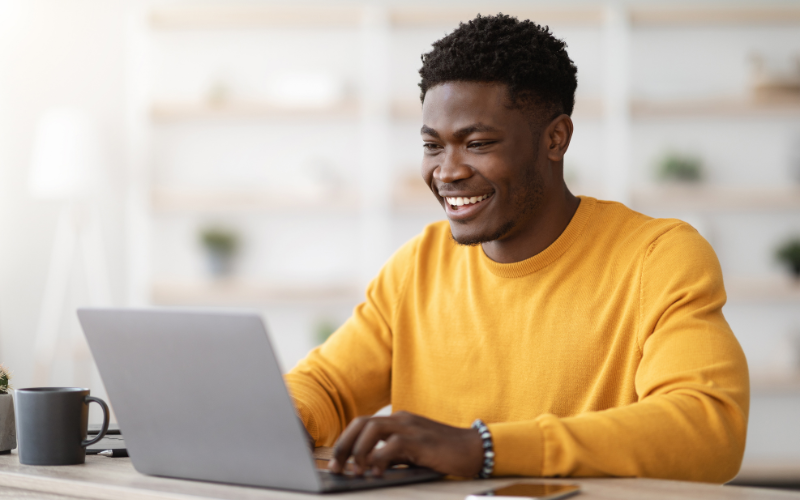 biblioteca de anúncios do facebook: imagem de um homem jovem negro, vestindo uma blusa amarela, digitando no notebook sobre a mesa