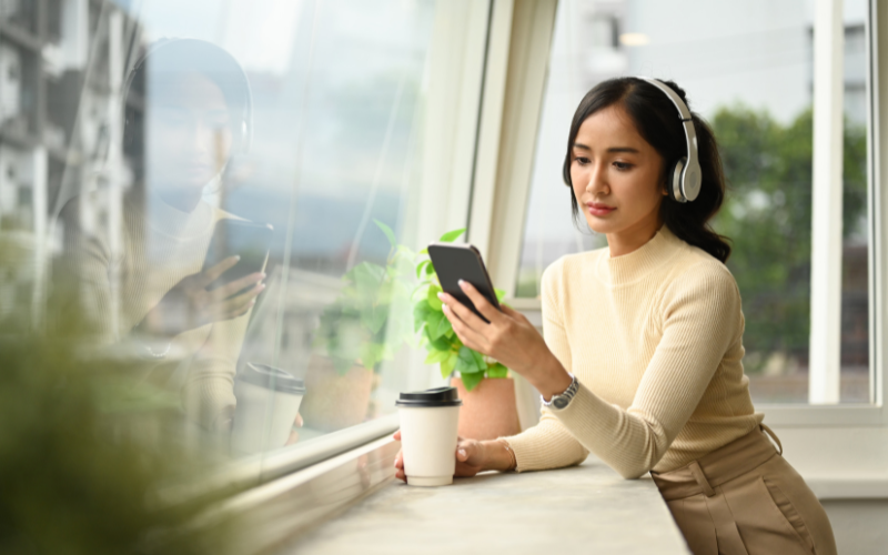 Deep Learning: imagem de uma jovem asiática olhando para a tela do seu celular e segurando um copo de café.