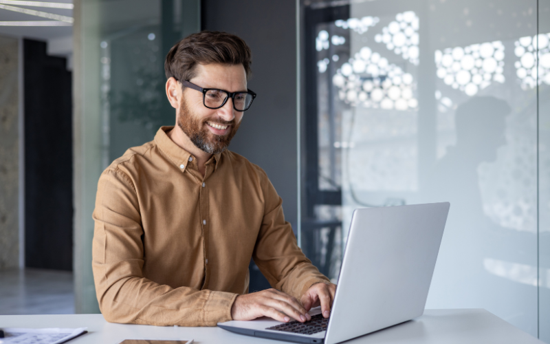 Ética e Inteligência Artificial: imagem de um homem branco, com a barba ruiva, vestido de social e sorrindo para o seu computador.