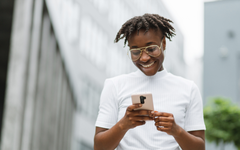 Inteligência Artificial e Experiência do Usuário: jovem negra, com blusa branca olhando para o seu smartphone